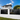 Modern black batten fence installed in front of a contemporary two-story house, with a white wall base, green lawn, and blue sky with clouds in the background.