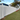 A long white batten fence installed along the side of a house, with green grass in front and trees and a blue sky in the background.
